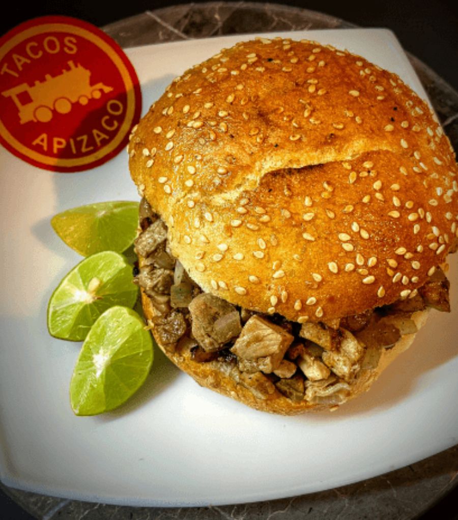 Cema de bistec: pan con ajonjolí relleno de bistec picado, con gajos de limón en un plato blanco.