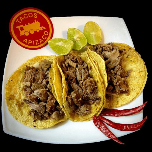 Tres tacos de maciza deshebrada en tortilla de maíz, con limones y chiles secos en un plato blanco.