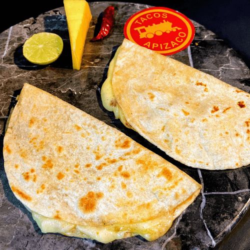 Dos quesadillas de tortilla de harina con queso fundido, con medio limón, un chile seco y un trozo de queso.