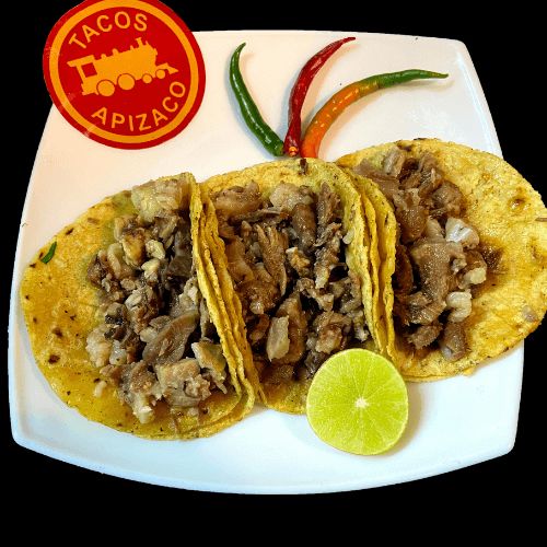 Tres tacos de surtido en tortilla de maíz, con chiles y medio limón en un plato blanco.